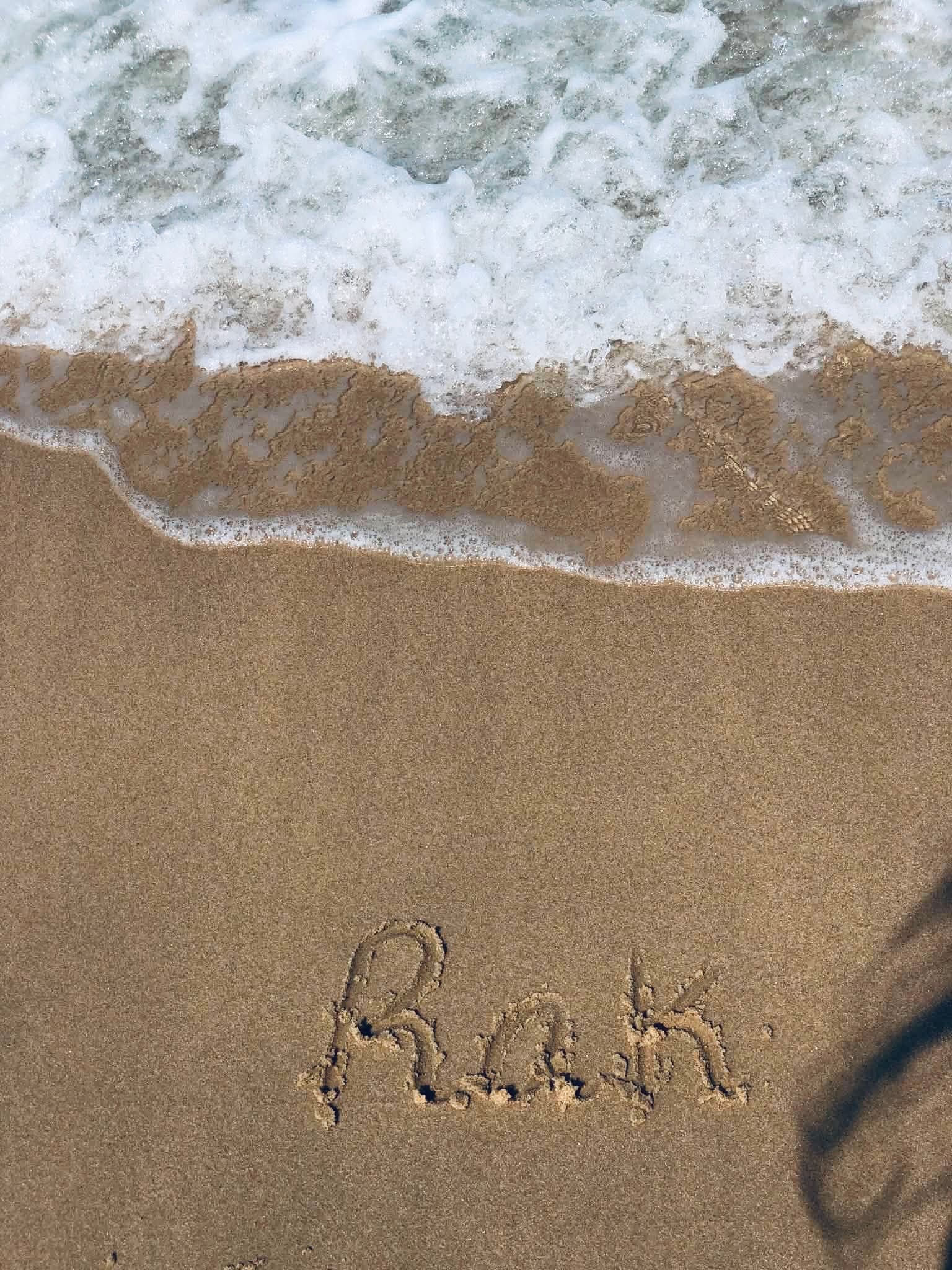 "Rak" written by hand in wet sand, a wave washing in behind it