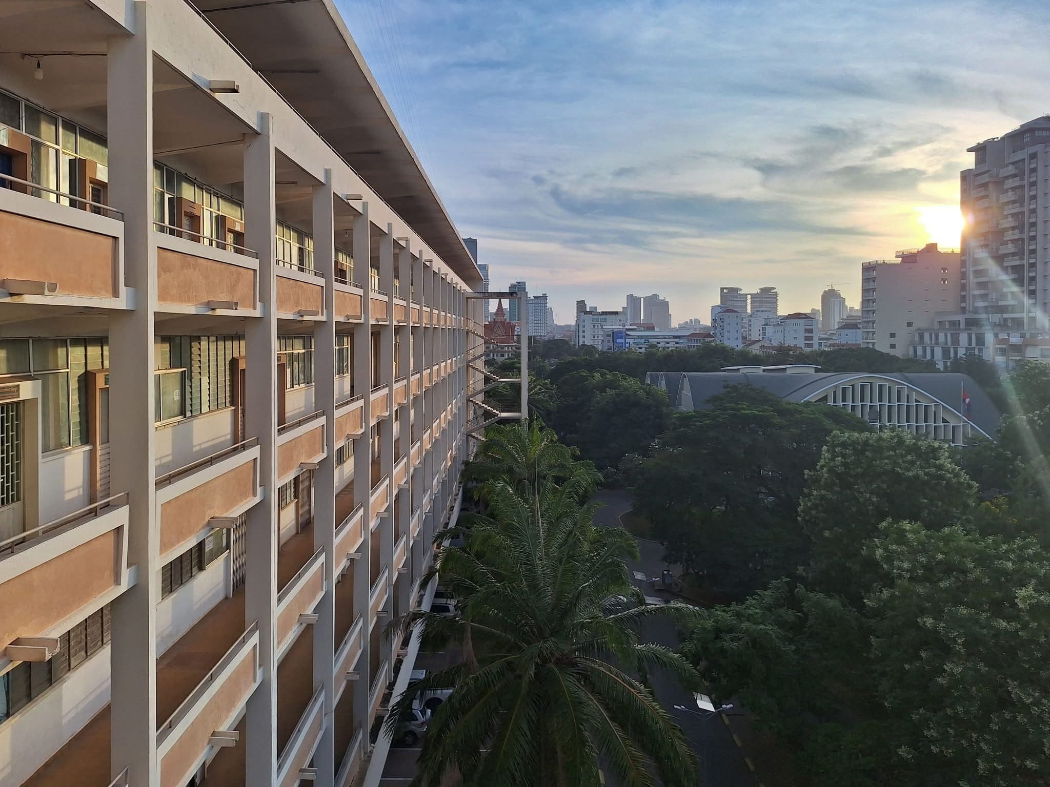 A long campus building at sunrise, with the Phnom Penh skyline in the distance